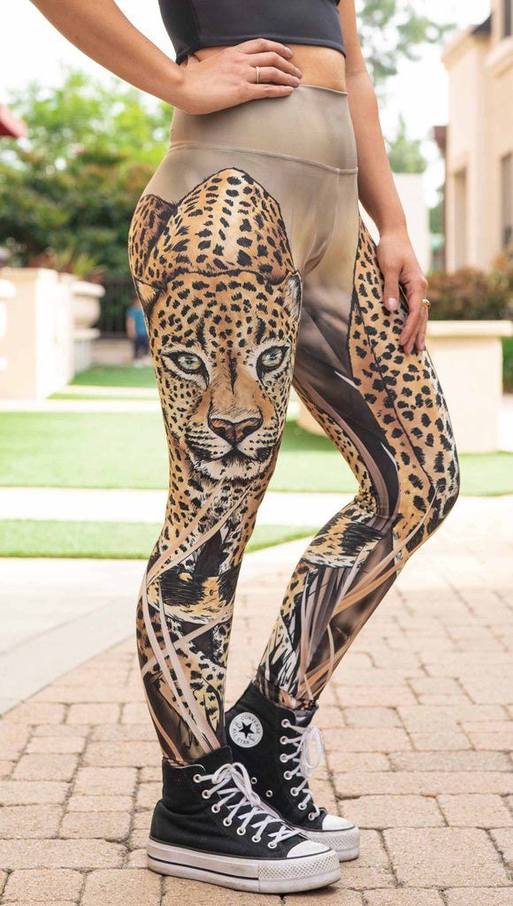 Model wearing WERKSHOP Leopard Legings. The leggings feature original and exclusive artwork of a Leopard walking through the brush. The leggings are all khaki and tan tones with little pops of green in the leopards eyes.