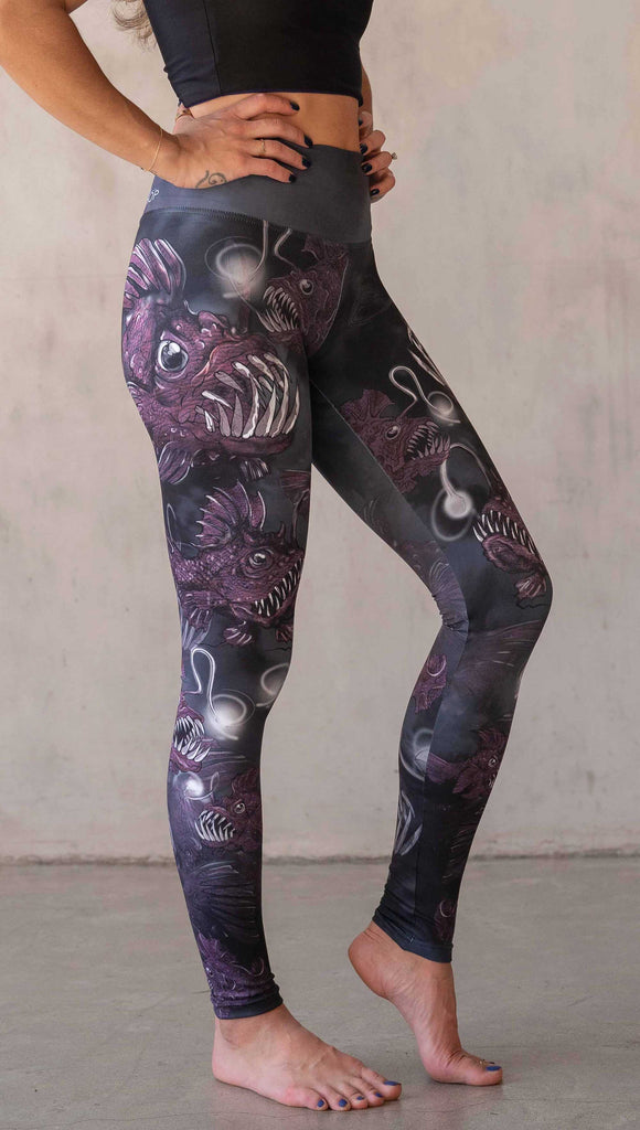 Girl wearing WERKSHOP Angler Fish Athleisure Leggings. The artwork on the leggings feature pink hued/textured angler fish over a black and gray airbrushed background
