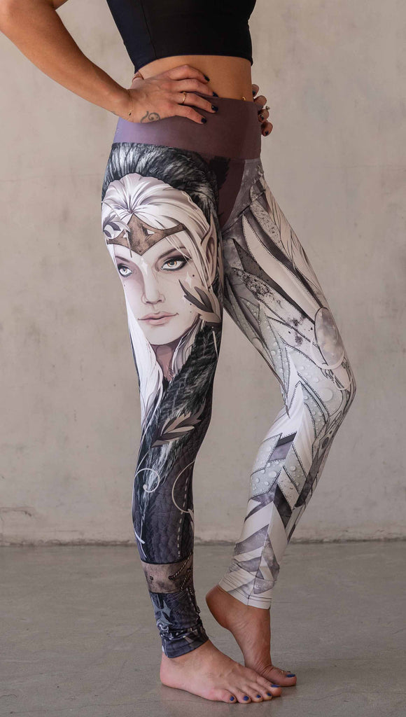 Model wearing WERKSHOP Elf + Sorceress Mashup leggings. The leggings are printed with original artwork by Chriztina Marie. One leg features a dark forest elf wearing a fur trimmed cloak. The other leg features a winter sorceress holding an orb with frosted purples and lavender tones.