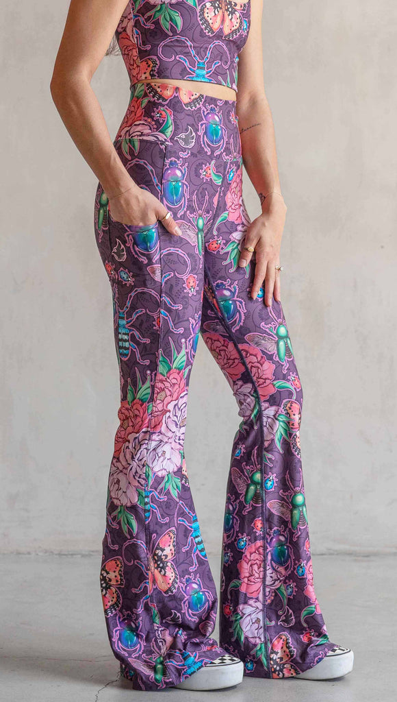 Side view of model wearing WERKSHOP Enchanted Garden EnviSoft Bell Bottom pants with Pockets. The fabric is printed with original artwork by our Female Founder, Chriztina Marie. The artwork printed not the fabric features Butterflies, Beetles and Peonies over a warm fuchsia with bright bold pops of color on each beetle and Butterfly.