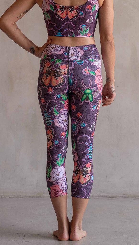 Back view of model wearing WERKSHOP Enchanted Garden Capri Length Triathlon Leggings. The fabric is printed with original artwork by our Female Founder, Chriztina Marie. The artwork printed not the fabric features Butterflies, Beetles and Peonies over a warm fuchsia with bright bold pops of color on each beetle and Butterfly.