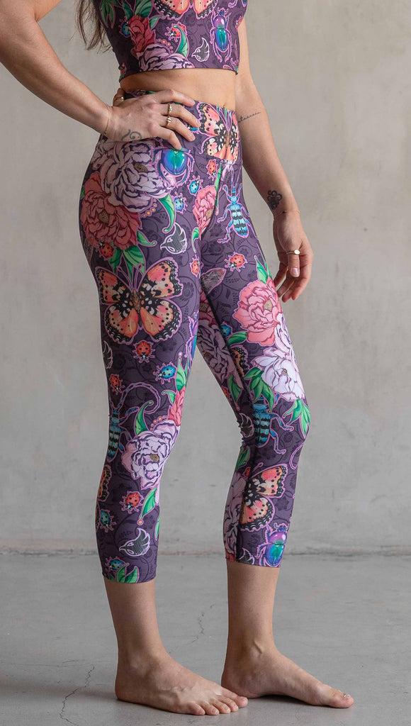 Side view of model wearing WERKSHOP Enchanted Garden Capri Length Triathlon Leggings. The fabric is printed with original artwork by our Female Founder, Chriztina Marie. The artwork printed not the fabric features Butterflies, Beetles and Peonies over a warm fuchsia with bright bold pops of color on each beetle and Butterfly.