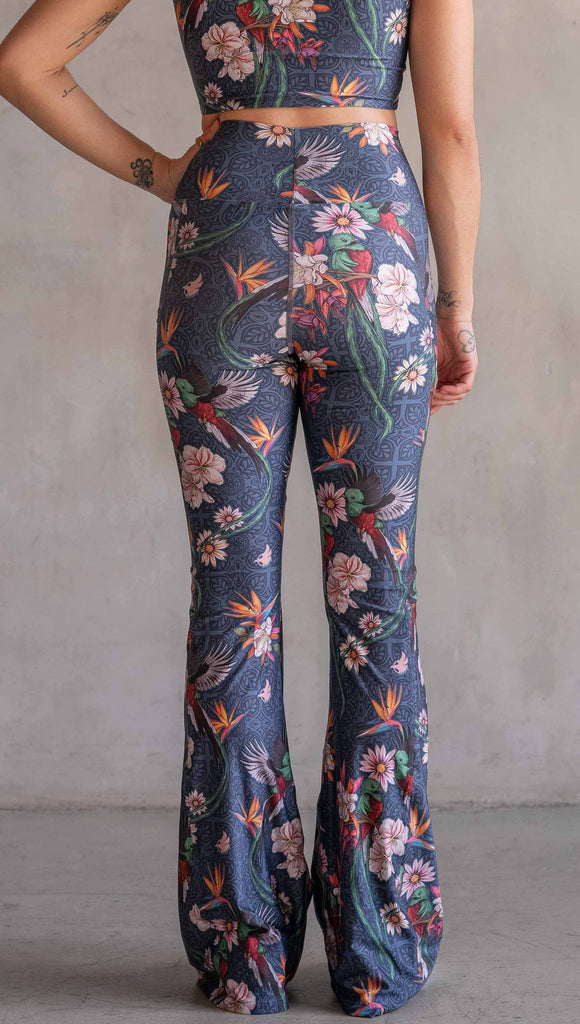 Model wearing WERKSHOP Quetzal Featherlight Bells. The leggings are printed with with original quetzal artwork with clusters of tropical flowers and birds of paradise over a blue background. The featherlight bells have pockets.