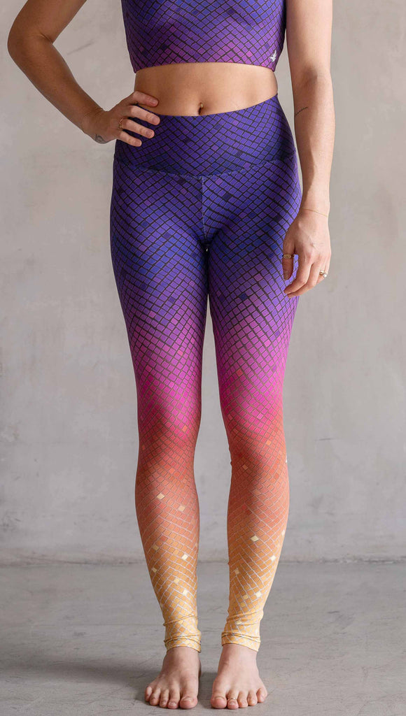 Model wearing WERKSHOP Rainbow Mosaic Athlesiure Leggings and matching top. The leggings are printed with what look like tiny mosaic tiles in an ombre effect from purple at the waistband, to pink at the knee ... then coral and a soft warm yellow at the leg opening.