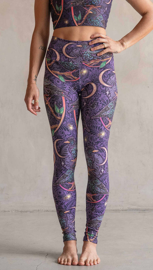 Front view of model wearing WERKSHOP Starlings Athleisure Leggings. The fabric is printed with original artwork by our Female Founder, Chriztina Marie. Featuring European Starlings perched on a branch near a crescent moon and fireflies. The colors are warm purples with pops of pink, gold and green.