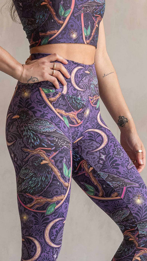 Zoomed in view of model wearing WERKSHOP Starlings Athleisure Leggings. The fabric is printed with original artwork by our Female Founder, Chriztina Marie. Featuring European Starlings perched on a branch near a crescent moon and fireflies. The colors are warm purples with pops of pink, gold and green.