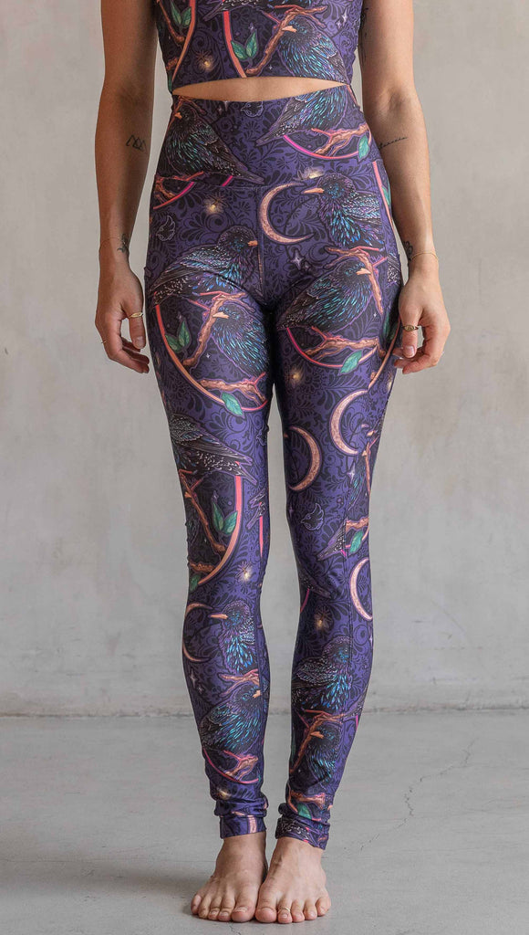 Front view of model wearing WERKSHOP Starlings EnviSoft leggings with pockets. The fabric is printed with original artwork by our Female Founder, Chriztina Marie. Featuring European Starlings perched on a branch near a crescent moon and fireflies. The colors are warm purples with pops of pink, gold and green.