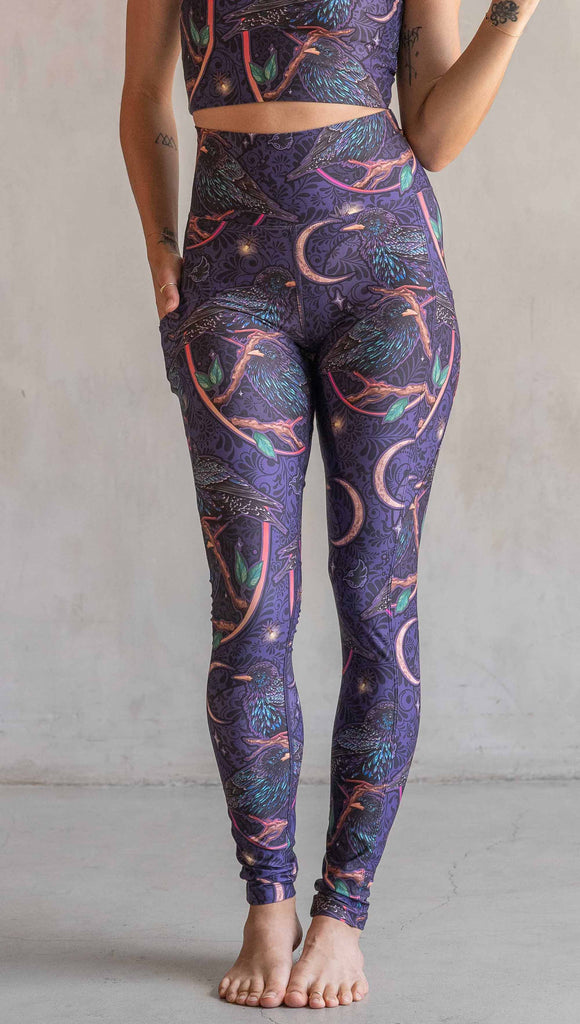 Front view of model wearing WERKSHOP Starlings EnviSoft leggings with pockets. The fabric is printed with original artwork by our Female Founder, Chriztina Marie. Featuring European Starlings perched on a branch near a crescent moon and fireflies. The colors are warm purples with pops of pink, gold and green.