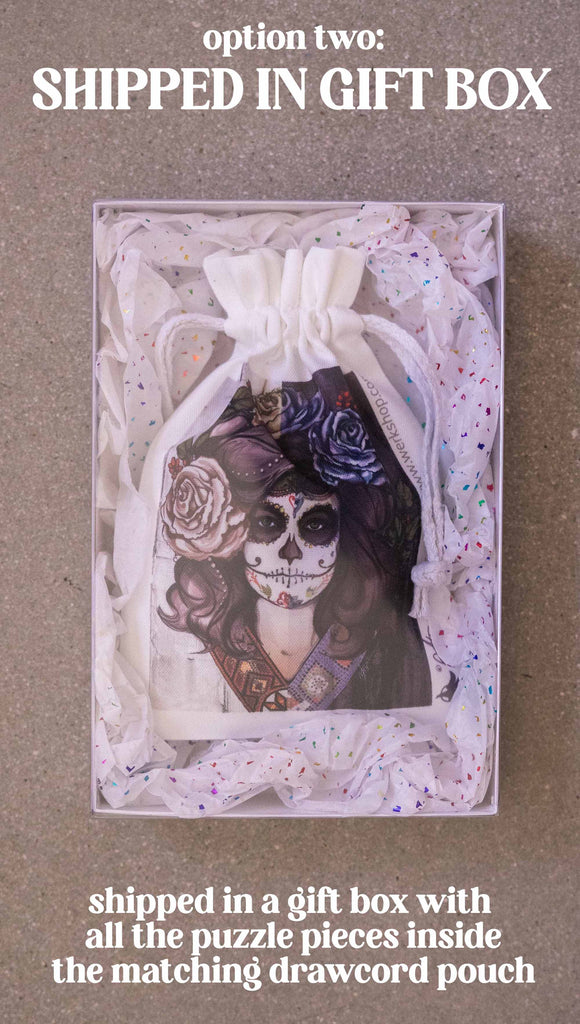 WERKSHOP Sugar Skull Mashup Puzzle. The artwork celebrates Dia De Los Muertos with a drawing of a girl wearing sugarskull makeup surrounded by a wreath of roses. Option 2: Shipped in a gift box with all the puzzle pieces inside the matching drawcord pouch.