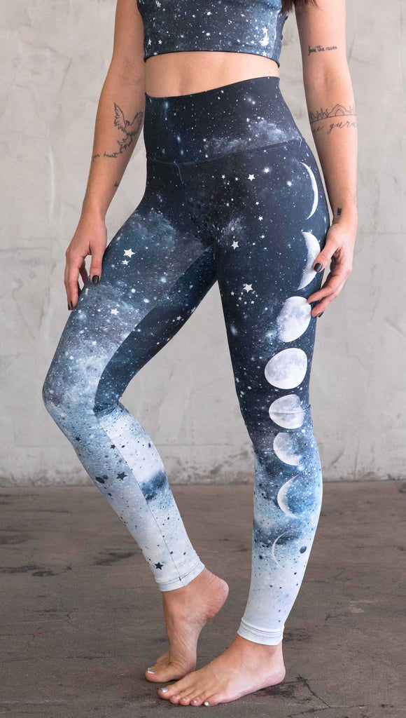 waist down view of a girl wearing our moon phases athleisure leggings - with the phases of the moon printed on the wearer's left leg on a starry night sky with all zodiac constellations in the background
