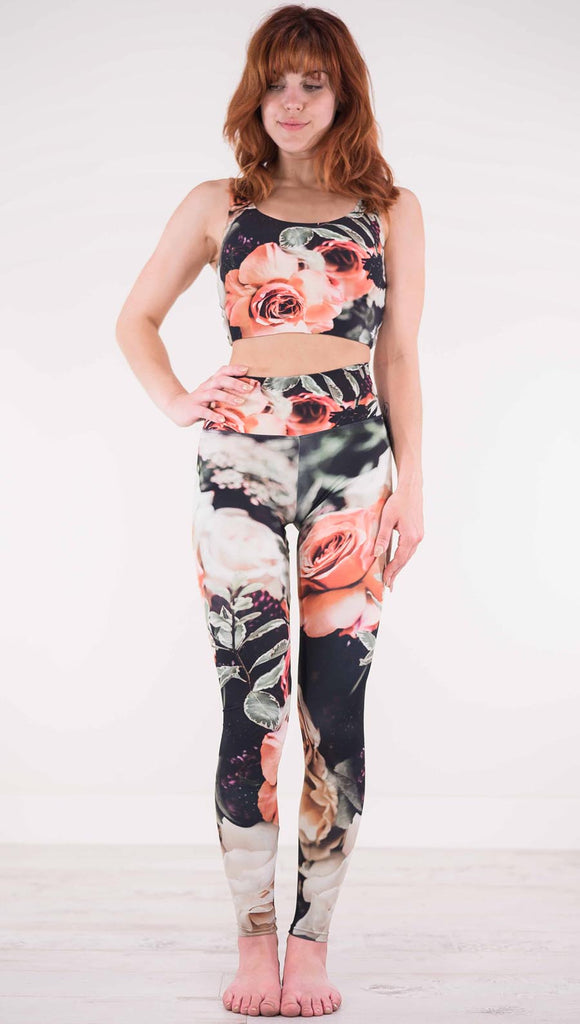 Front view of model wearing black athleisure leggings with pink and white roses and leafy greens throughout