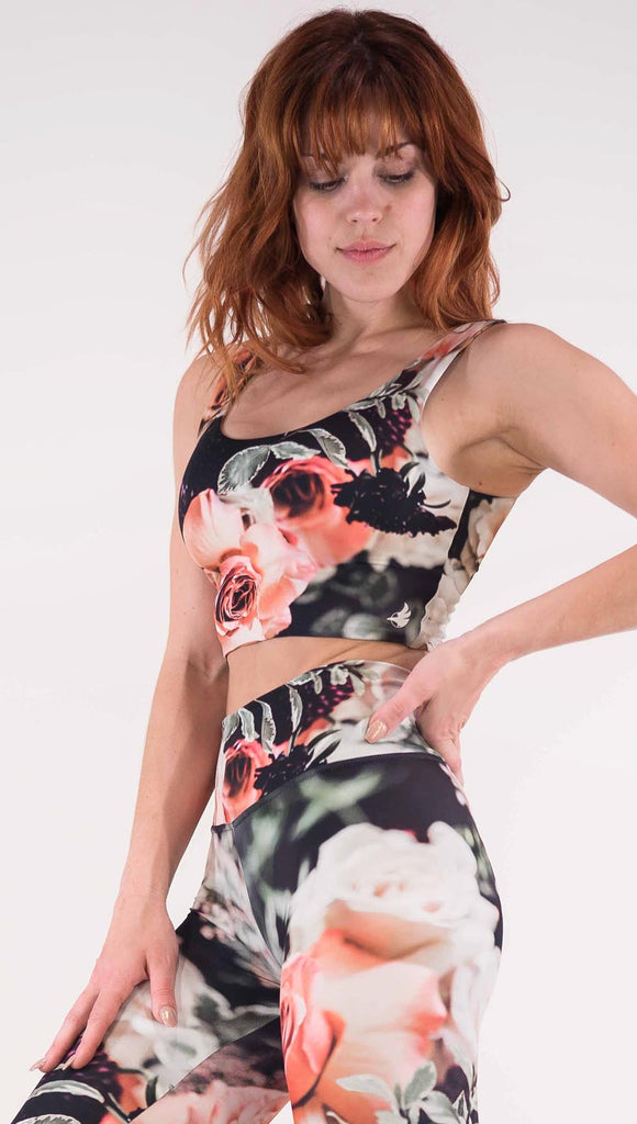 Left view of model wearing the Bodacious Bouquet crop top. It is in a black color with pink and white roses and leafy greens throughout