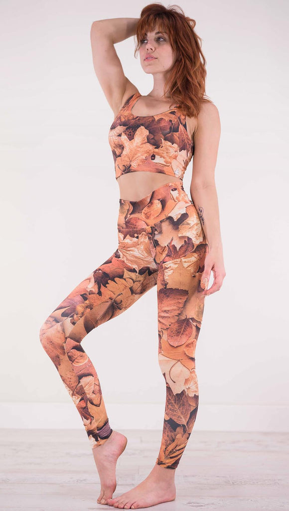 Left view of model wearing athleisure leggings that have different shades of orange autumn leaves