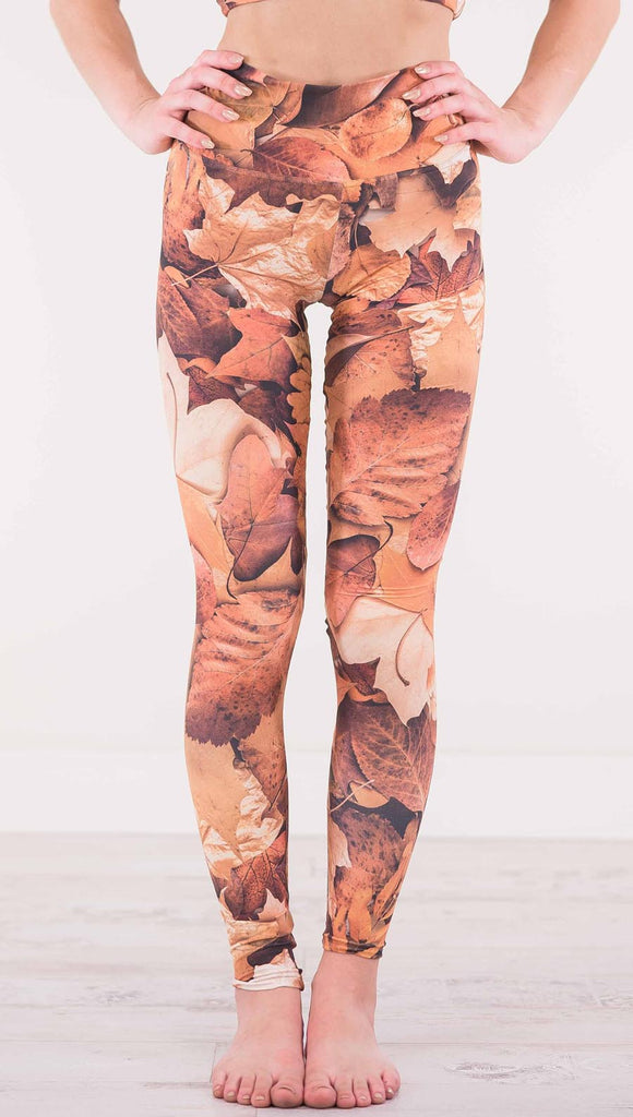 Front view of model wearing athleisure leggings that have different shades of orange autumn leaves