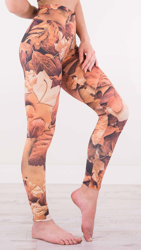 Right view of model wearing athleisure leggings that have different shades of orange autumn leaves
