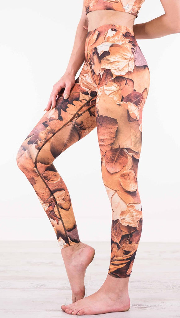 Enhanced left view of model wearing triathlon leggings that have different shades of orange autumn leaves