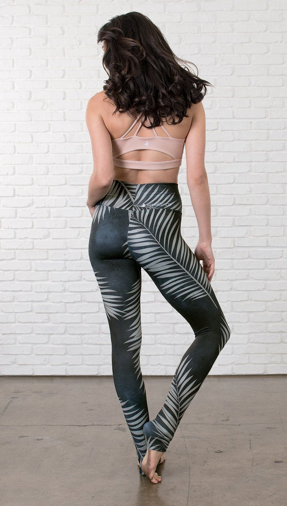 back view of model wearing full length black leggings with white palm design and sports top