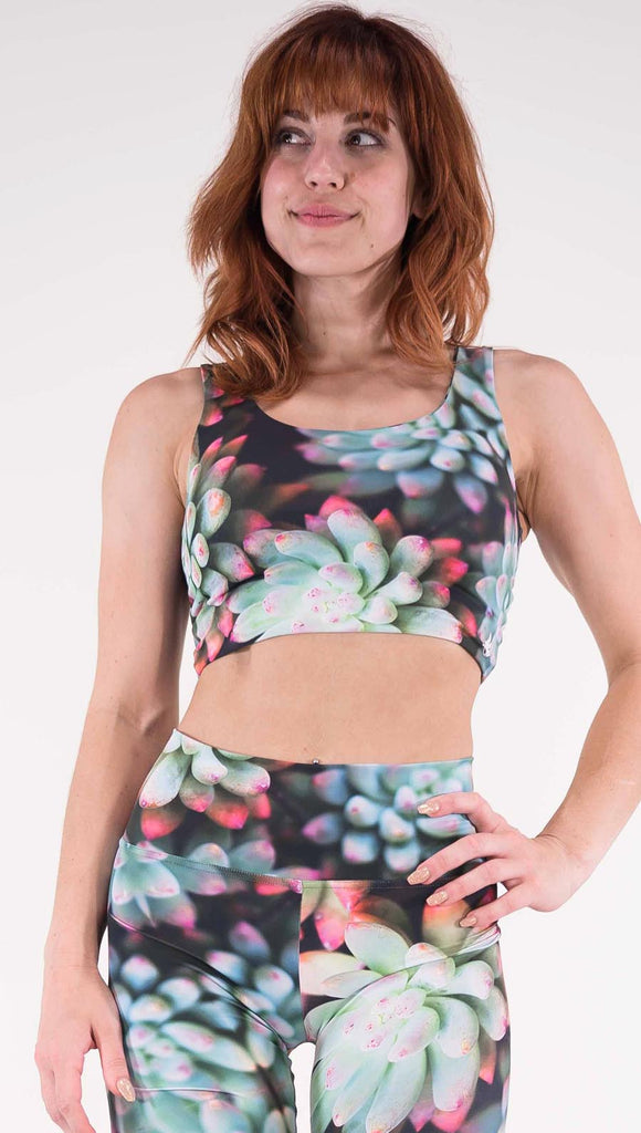 Front view of model wearing the reversible Coachella Sunset Top. This is the Coachella Sunset side, it is a black crop top with green succulent plants with pink tips throughout