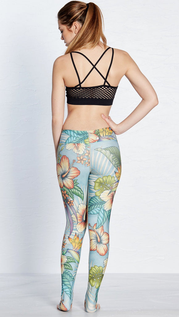 back view of model wearing printed full length leggings with tropical floral design and blue background