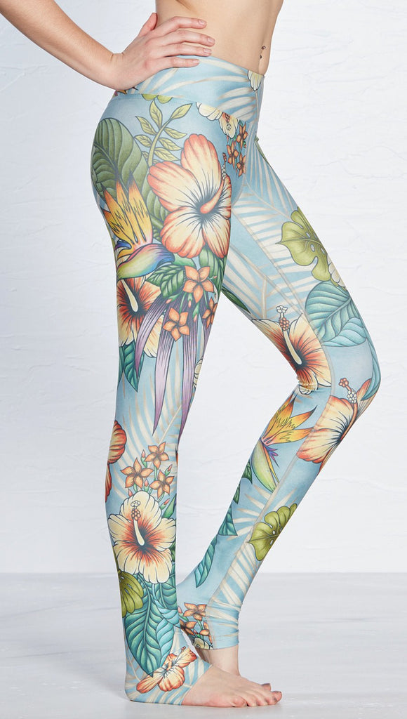 close up right side view of model wearing printed full length leggings with tropical floral design and blue background