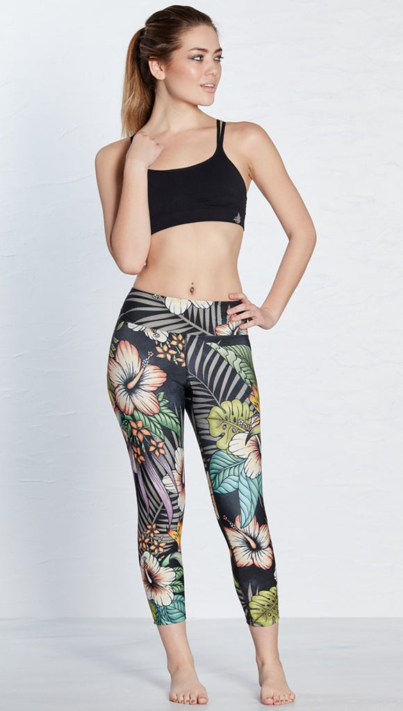 front view of model wearing printed capri leggings with tropical floral design and black background