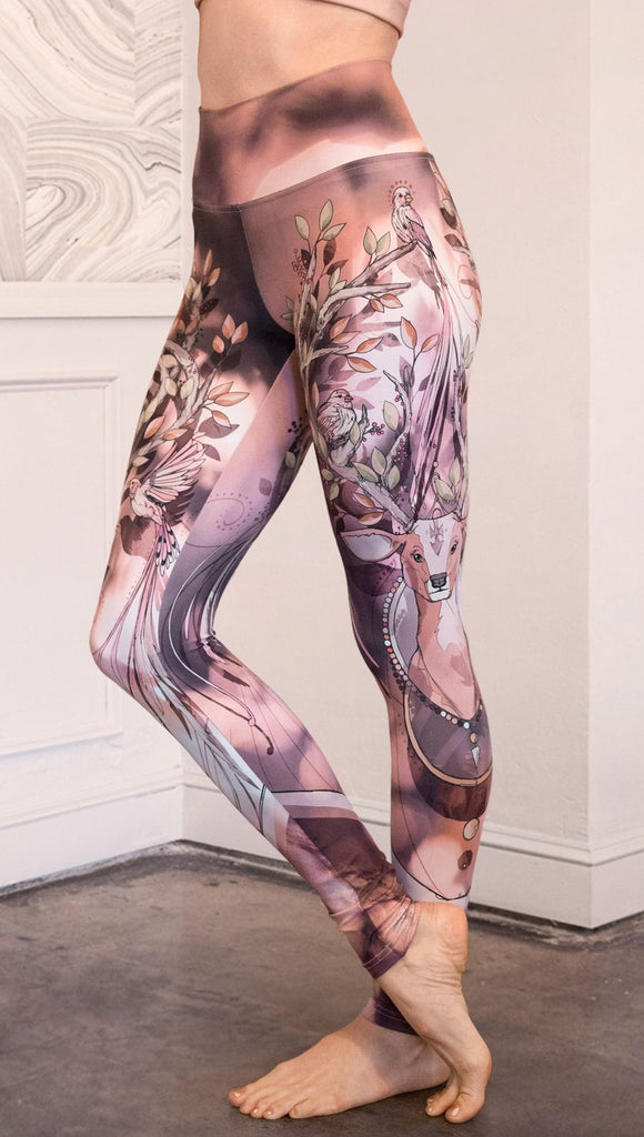 Left view of model wearing full length athleisure leggings with a deer on it. They are a purple and orange color with tree branches as the antlers and birds on the antlers
