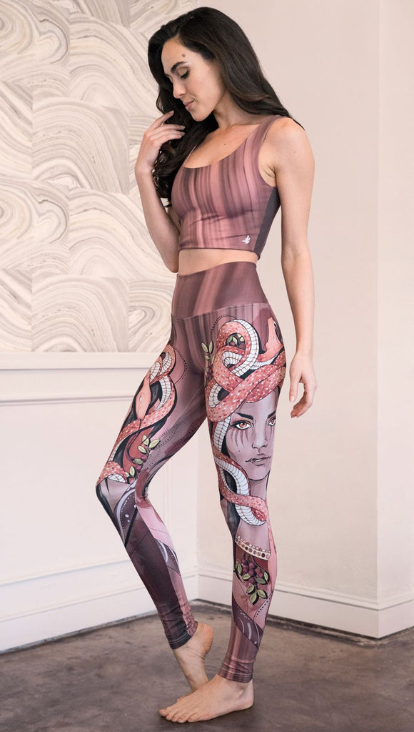 Slightly turned view of the model wearing full length athleisure leggings with a mauve color medusa head and red, white, and black snakes