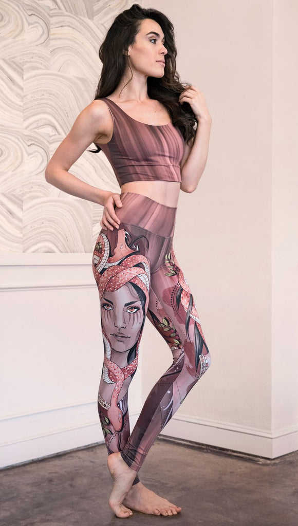Slightly turned right side view of the model wearing full length athleisure leggings with a mauve color medusa head and red, white, and black snakes