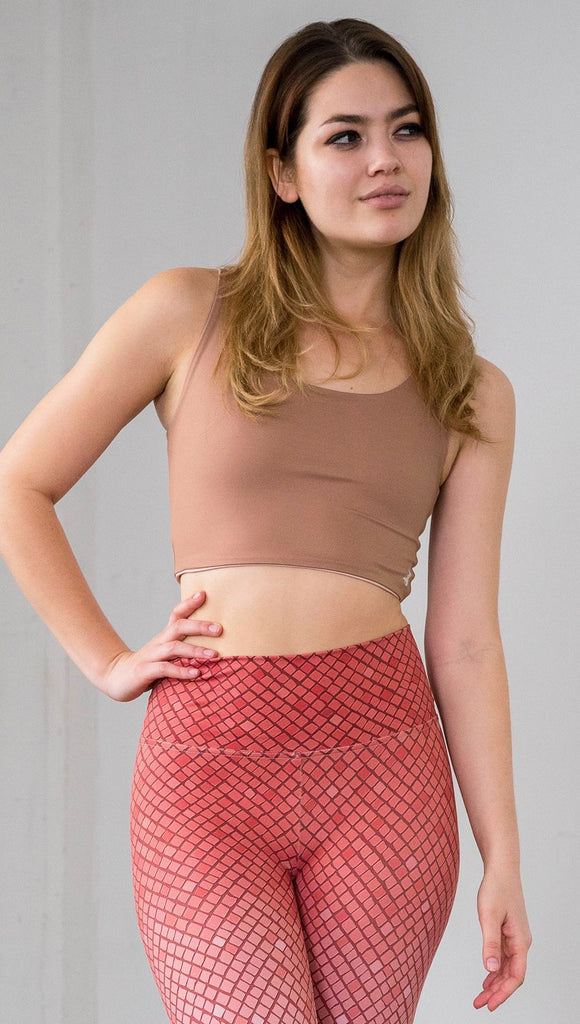 Three quarter length front view of model wearing a reversible light brown/medium skin tone crop top with a beige/lighter skin top on the inside