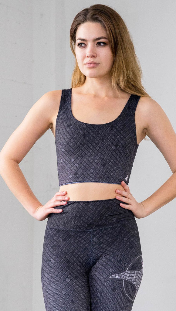 Three quarter length front view of a model wearing a dark gray mosaic tile print reversible crop top with blue mosaic tile print on the other side 