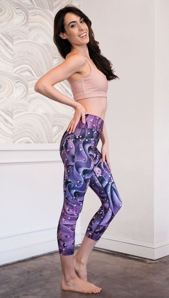 right side view of model wearing cupcake themed capri leggings with purple and royal blue frosting and rainbow colored sprinkle design
