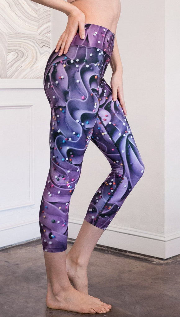 closeup right side view of model wearing cupcake themed capri leggings with purple and royal blue frosting and rainbow colored sprinkle design