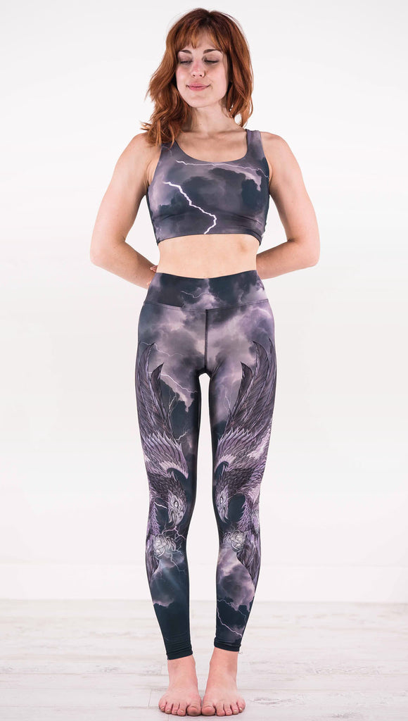 Front view of model wearing dark gray triathlon leggings with a large purple bird across each leg with lightning in the background
