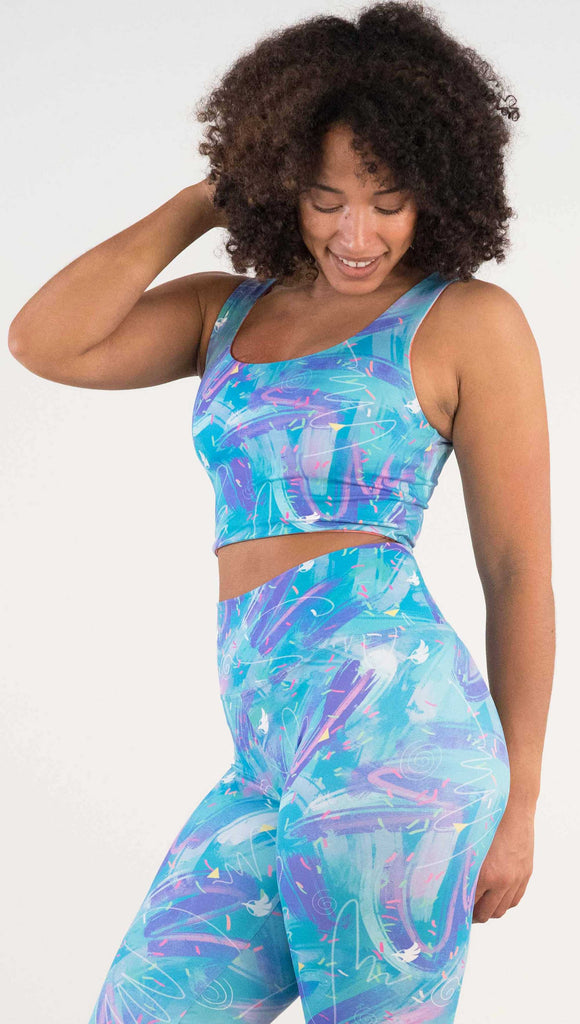 Model wearing WERKSHOP Teal/Salmon Scribble Reversible Top with whimsical brushstrokes and little confetti and eagle logos scattered throughout. (Teal on one side and Salmon on the other side)
