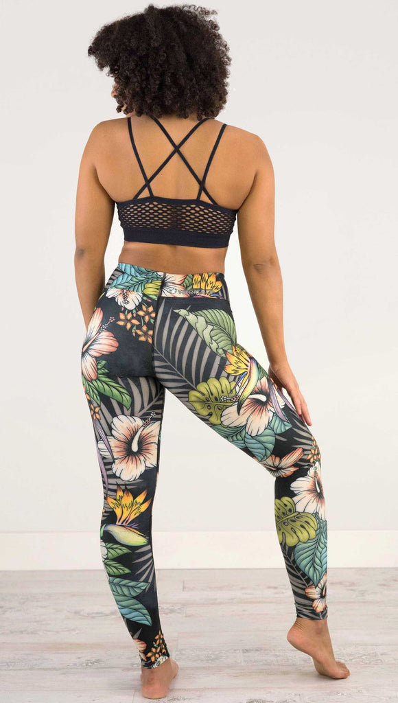 Back view of model wearing WERKSHOP Floral Night Full Length Triathlon Leggings. The artwork on the leggings has tropical flowers (bird of paradise, hibiscus and palm leaves) on a distressed black background.