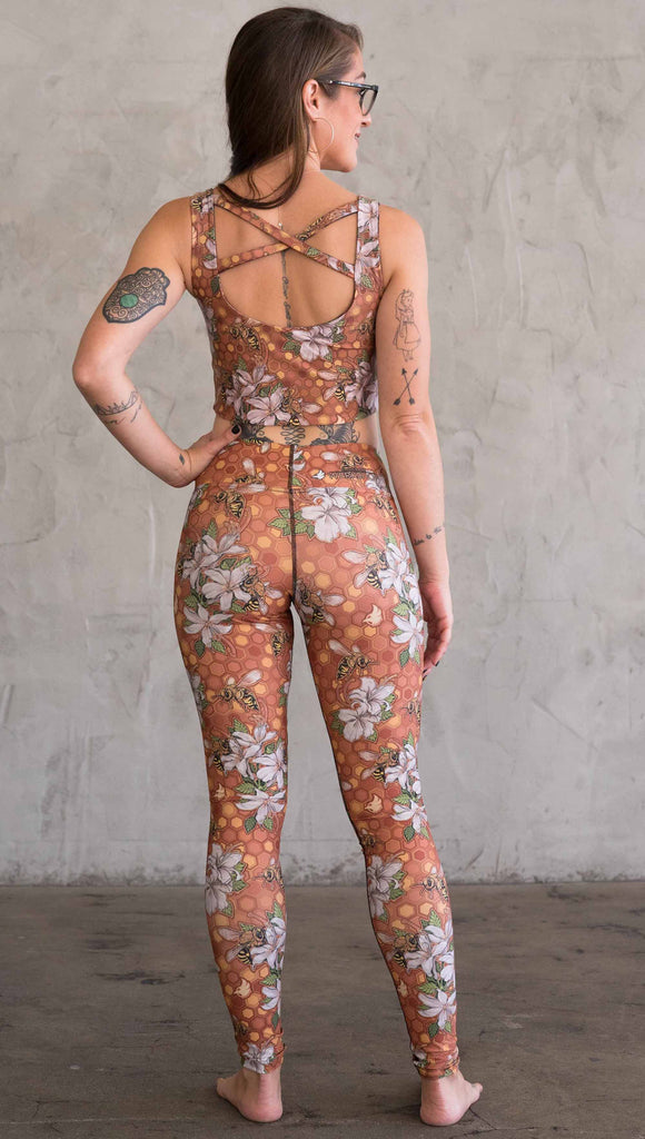 Full body back view of model wearing WERKSHOP Honeybees leggings in triathlon fabric. The artwork has clusters of honeybees and flowers.