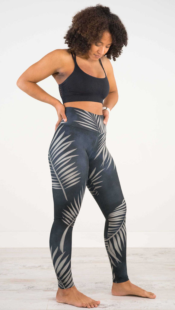 Full body side view of model wearing WERKSHOP Black Palms leggings. The leggings are printed with a mostly black watercolor effect with grayish palm frond silhouette wrapping the body.