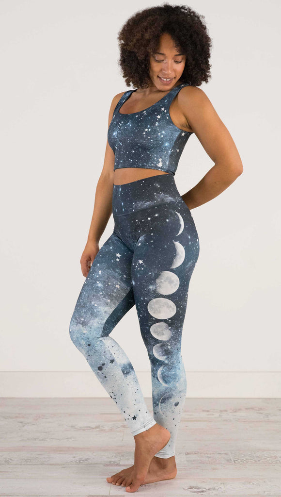 Full body side view of a girl wearing our moon phases athleisure leggings - with the phases of the moon printed on the wearer's left leg on a starry night sky with all zodiac constellations in the background