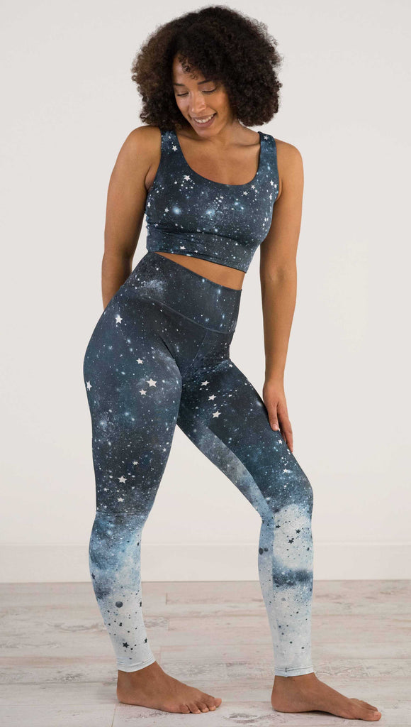 Full body side view of a girl wearing our moon phases athleisure leggings - with the phases of the moon printed on the wearer's left leg on a starry night sky with all zodiac constellations in the background
