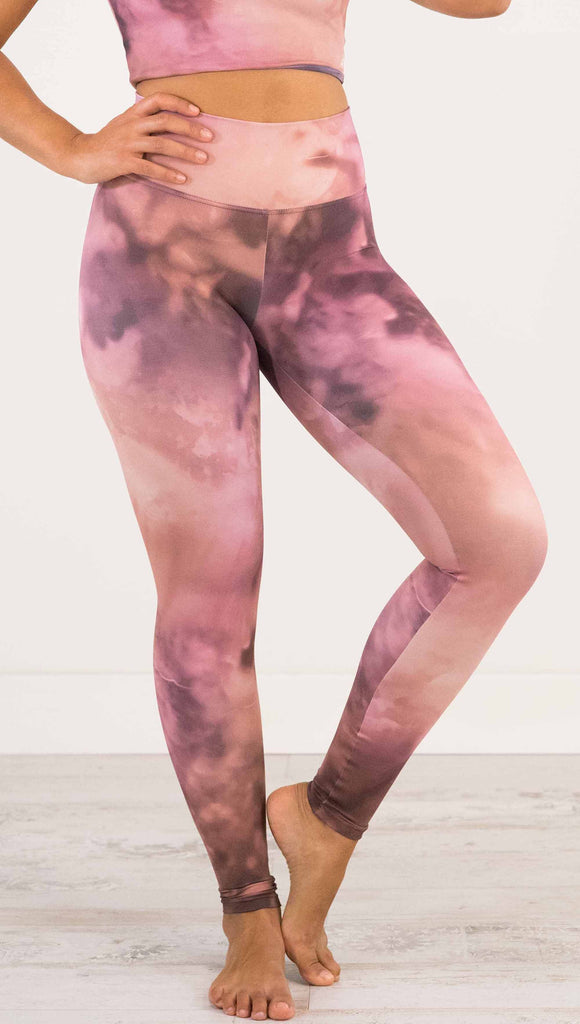 Waist down front view of model wearing WERKSHOP Rose Quartz Athleisure Leggings. The leggings are printed with a warm rose/mauve and peachy watercolor effect with our eagle logo printed on the wearers outside left calf.