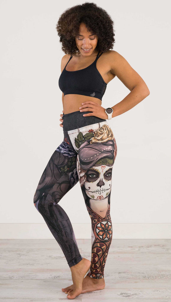 Full body front view of model wearing WERKSHOP Sugar Mashup Athleisure Leggings. The leggings are printed with original sugarskull themed artwork. The wearers left leg features "Remix", a romantic lighter version of the artwork with mauve roses in her hair. The other leg is printed with Dark Sugar, an edgier version of the same artwork with blue flowers in her hair. 