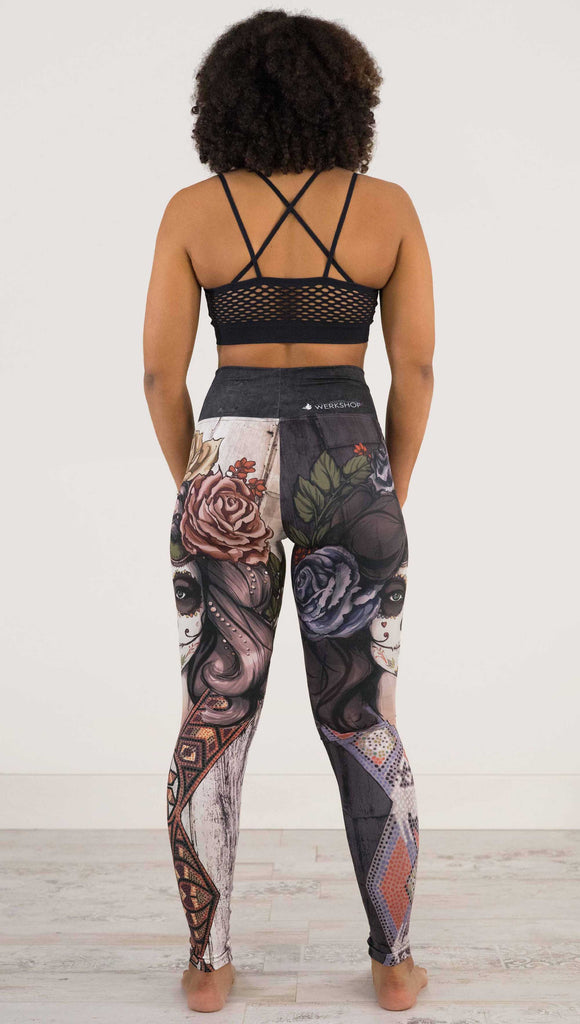 Full body back view of model wearing WERKSHOP Sugar Mashup Athleisure Leggings. The leggings are printed with original sugarskull themed artwork. The wearers left leg features "Remix", a romantic lighter version of the artwork with mauve roses in her hair. The other leg is printed with Dark Sugar, an edgier version of the same artwork with blue flowers in her hair. 