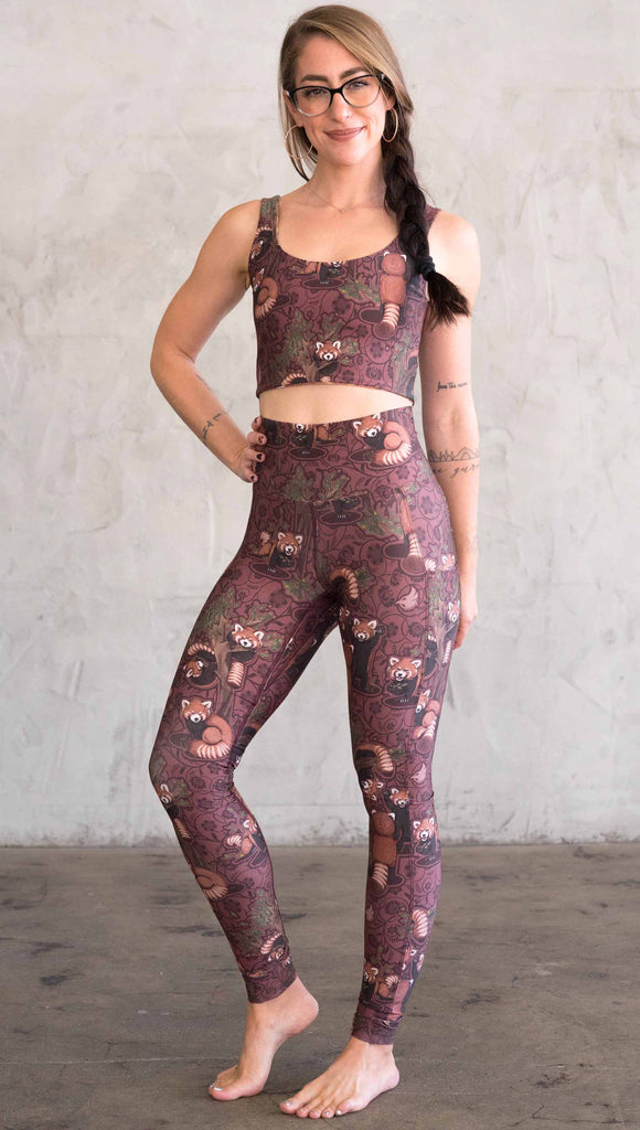 Full body front view of model wearing WERKSHOP Red Panda Leggings. The artwork is dark red with clusters of cute red pandas playing on trees. The leggings have phone pockets on both legs.