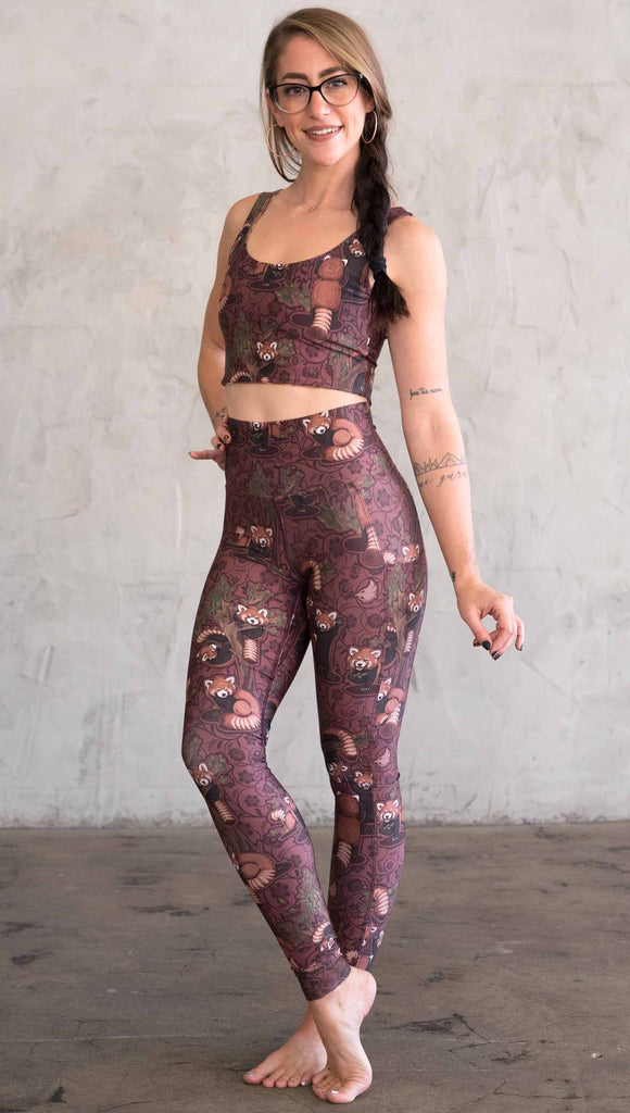 Full Body Front view of model wearing WERKSHOP Red Panda Leggings. The artwork is dark red with clusters of cute red pandas playing on trees. The leggings have phone pockets on both legs.
