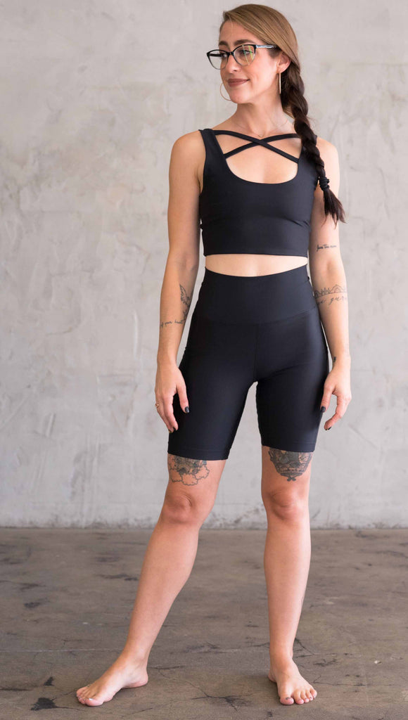 Full body front view of model wearing WERKSHOP bicycle length shorts in featherlight fabric. Black color with side cell phone pockets and a small eagle logo on the wearers left side