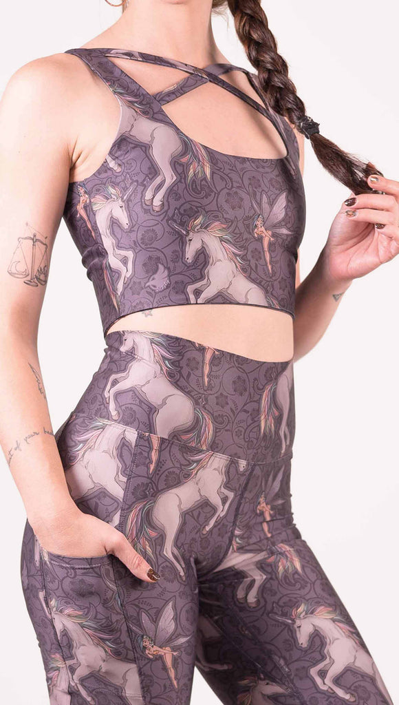 Zoomed in view of model wearing WERKSHOP featherlight bell bottom flares with Original Unicorn artwork. The unicorns have soft rainbow colored hair and a small pixie friend over a purple background. The pants have large pockets on each hip large enough to hold a phone.