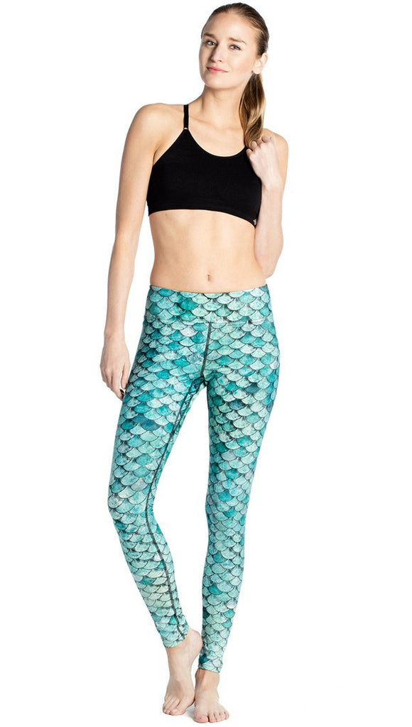 front view of model wearing teal mermaid / fish scale printed full length leggings