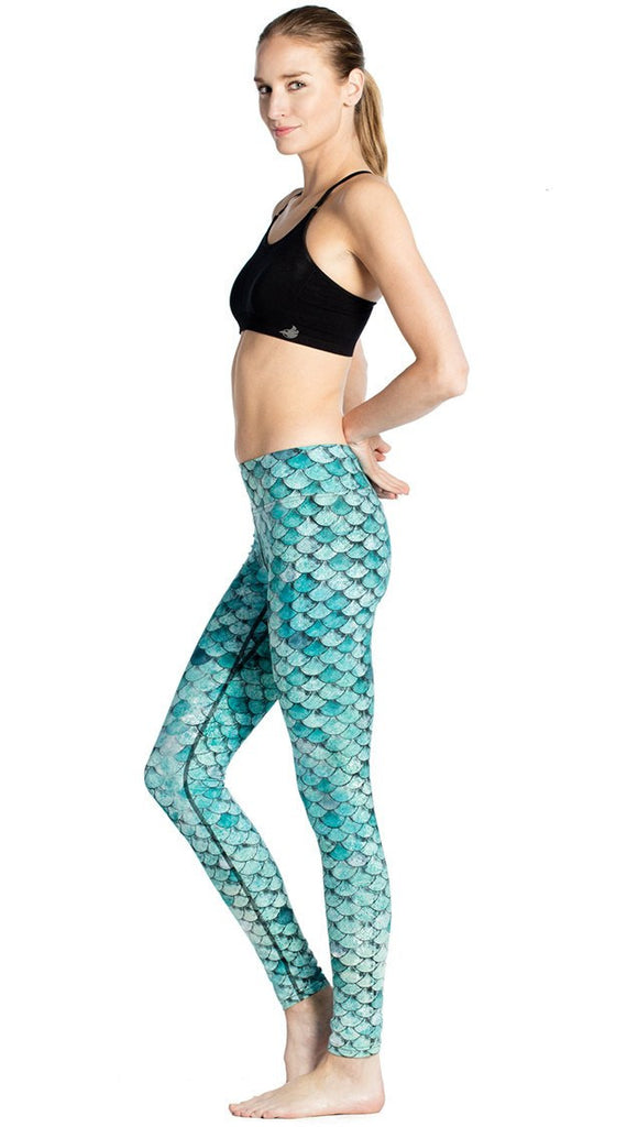 left side view of model wearing teal mermaid / fish scale printed full length leggings