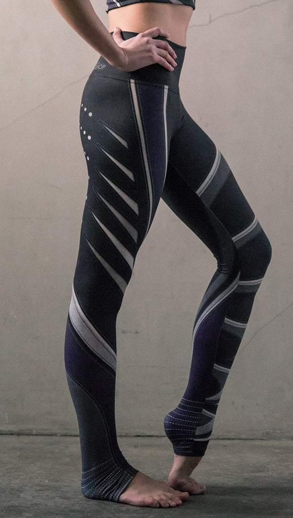 Right side view of model wearing black printed full-length leggings with purple and gray stripe design