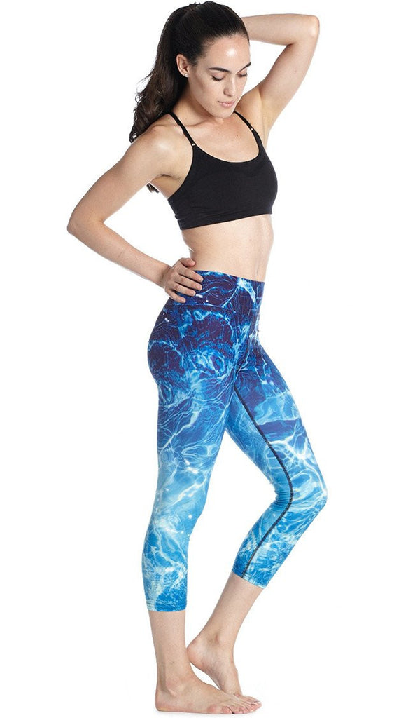 right side view of model wearing water / ocean themed printed capri leggings and black sport top